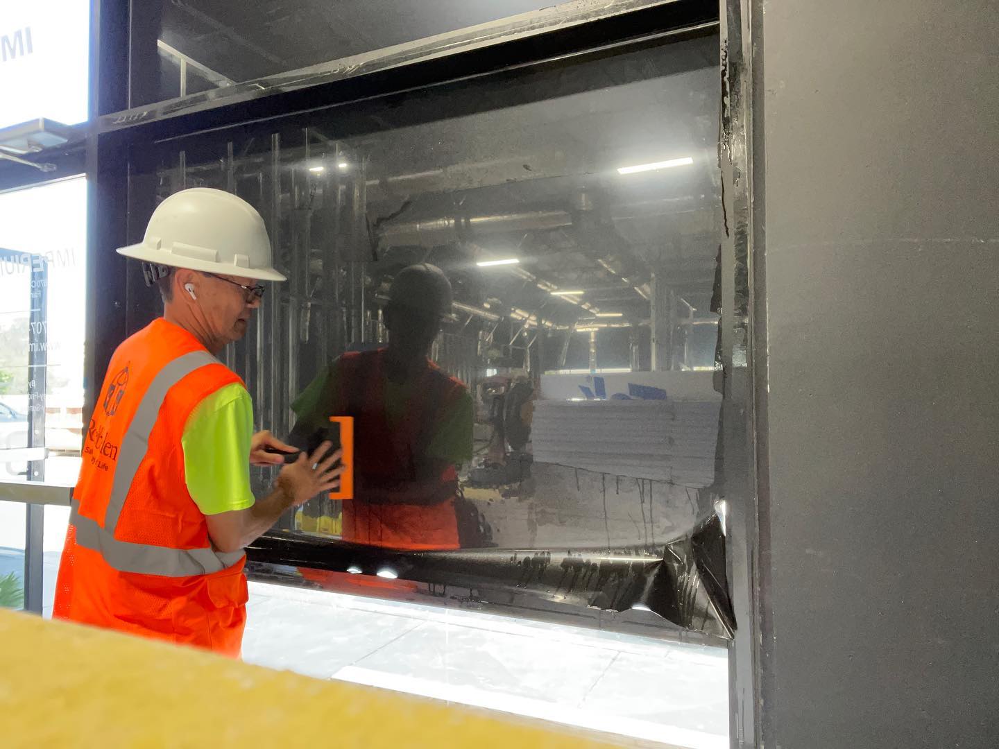 Installer in a hard hat and safety vest applying film to office glass